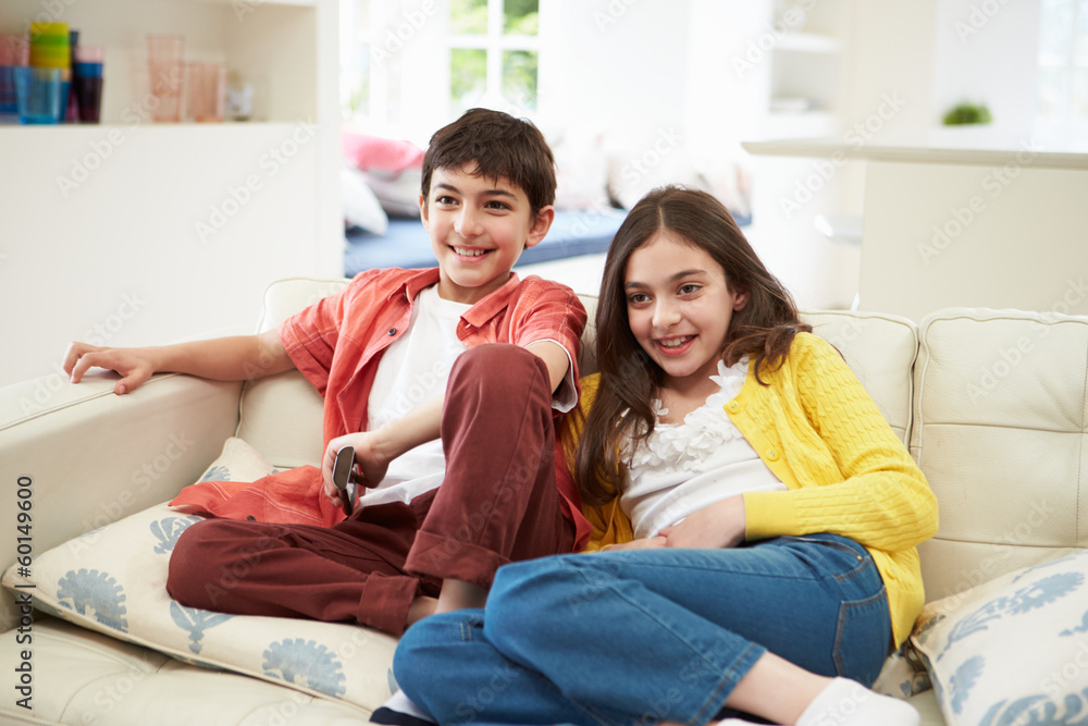 Two Hispanic Children Sitting On Sofa Watching TV Together