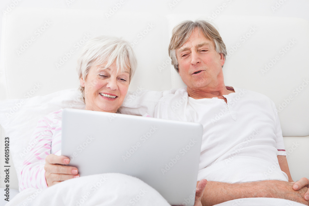Senior Couple On Bed Looking At Laptop