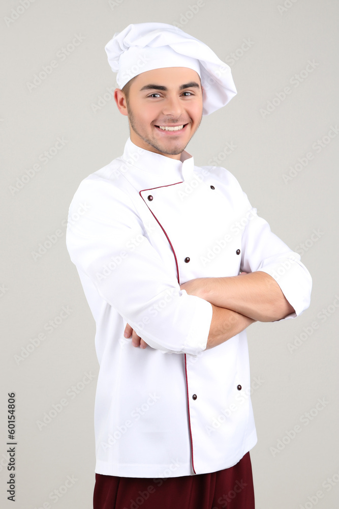 Professional chef in white uniform and hat, on gray background