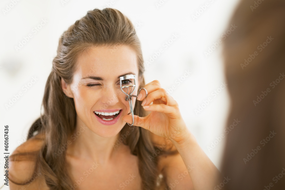 Young woman using eyelash curler in bathroom Young woman using eyelash curler in bathroom
