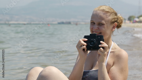 Smiling woman taking a photo at the seaside with her vintage photo