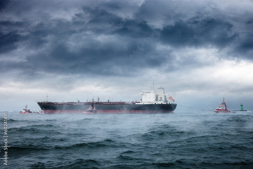 A tanker and tugboats on sea during a violent blizzard.