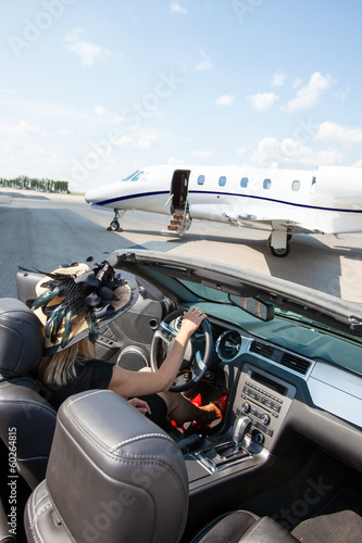 Fototapeta Naklejka Na Ścianę i Meble -  Woman In Convertible With Private Jet At Terminal
