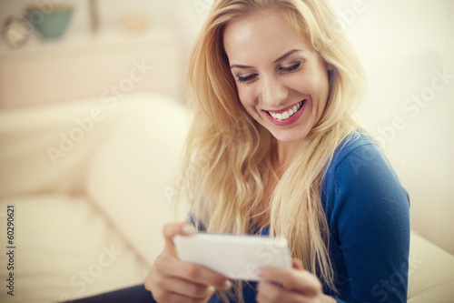 Happy young woman with white mobile phone on sofa