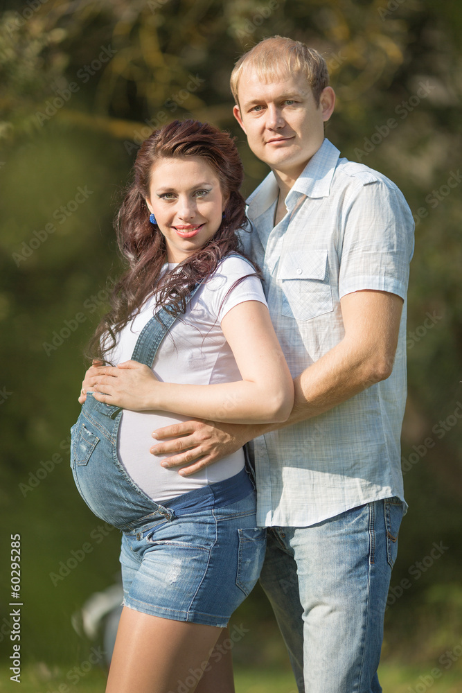 Obraz premium Young man with his pregnant wife posing on open air