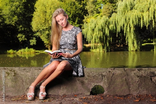 Blonde girl with book on green background of city park