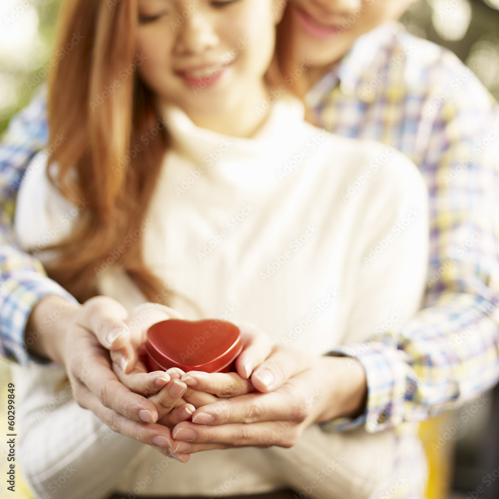 young loving couple holding heart-shaped gift box young loving couple holding heart-shaped gift box