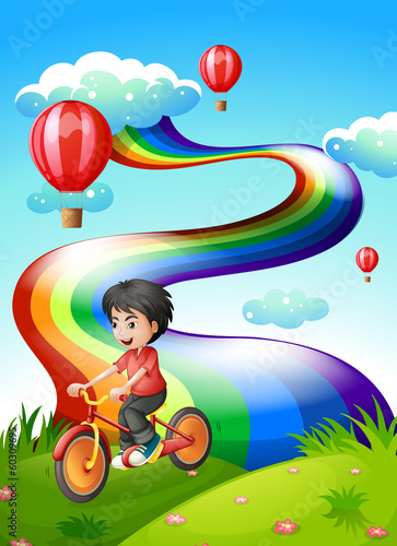 A boy biking at the hilltop with a rainbow