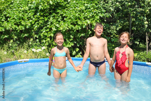 Two girls and a boy standing holding hands in a pool
