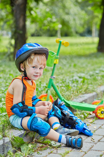 Little scooterist in protective equipment rests sitting on curb photo