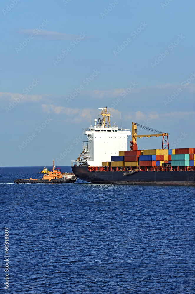 Fototapeta premium Tugboat assisting container cargo ship to harbor quayside