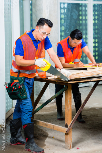 Builder sawing a wood board of building or construction site