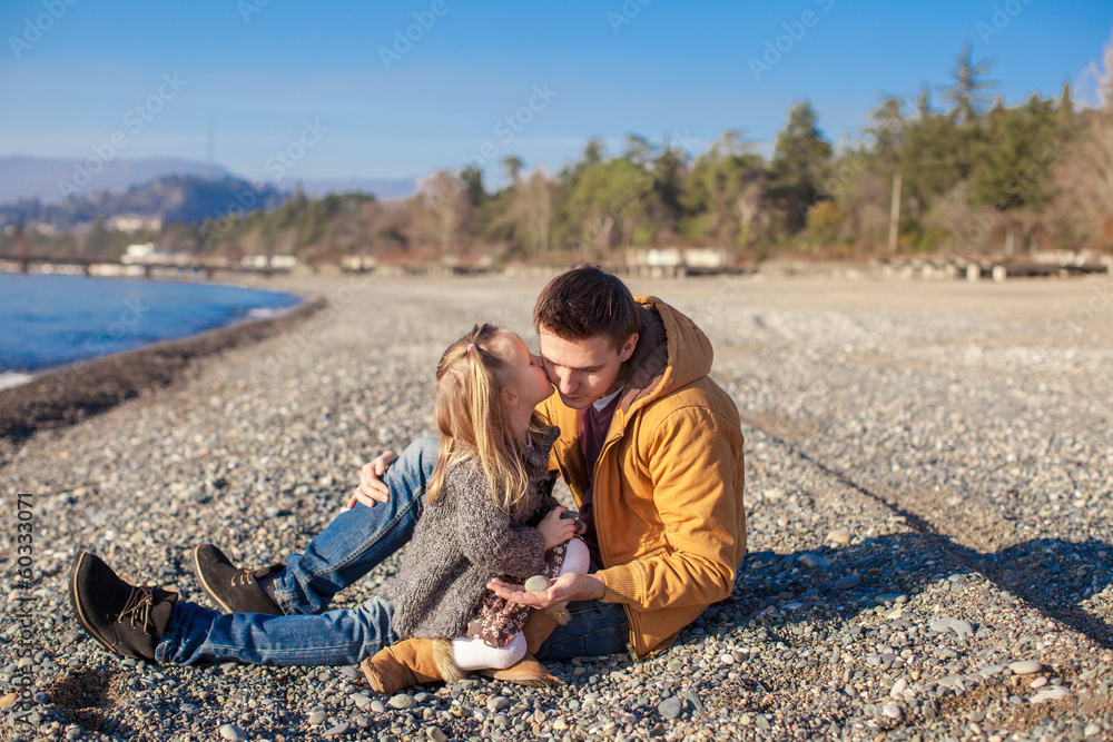 Young father holding little daughter kissing him at beach in