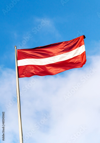 Flag of Latvia above blue sky with clouds
