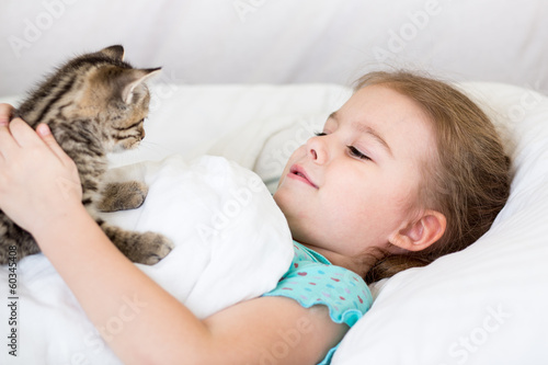 Child girl with kitten laying in the bed