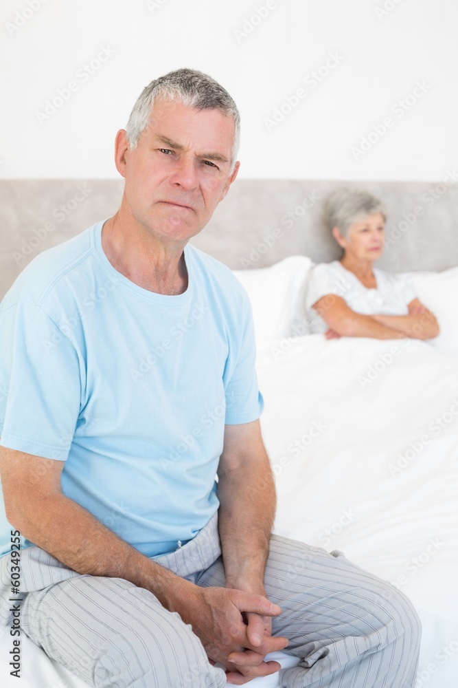 Angry senior man on bed with woman in background Angry senior man on bed with woman in background