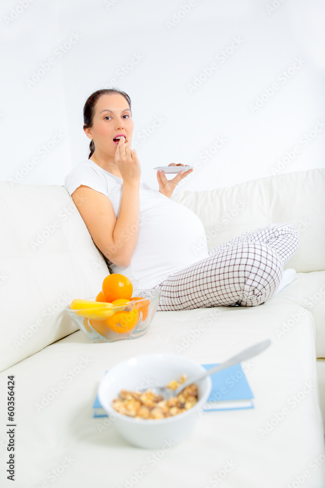 Beautiful pregnant eating chocolate on sofa at home
