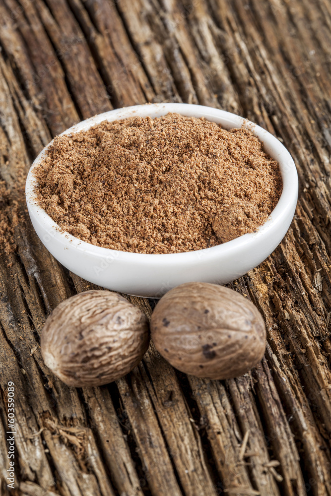 Spice nutmeg in whole and ground in white bowl Spice nutmeg in whole and ground in white bowl