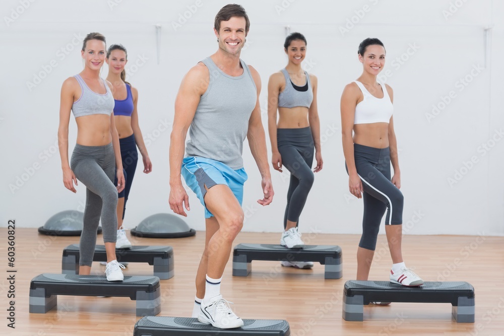 Instructor with fitness class performing step aerobics exercise Instructor with fitness class performing step aerobics exercise
