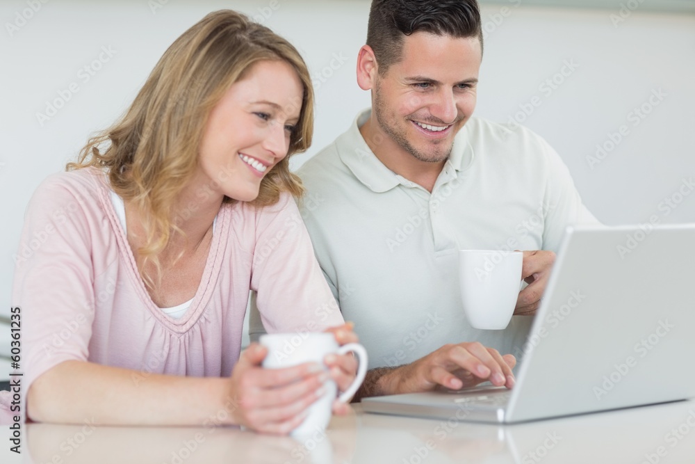 Couple with coffee mugs using laptop at table Couple with coffee mugs using laptop at table