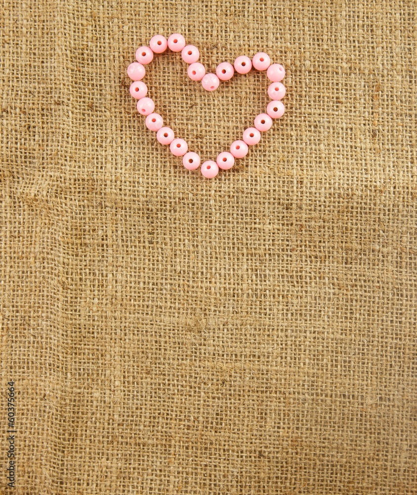 Beads arrange as heart shape on hemp background