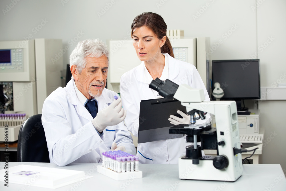 Scientist Reading Sample While Colleague Taking Notes