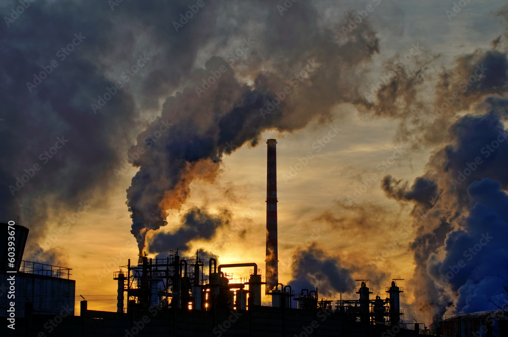 Chimneys and dark smoke over chemical factory at sunset