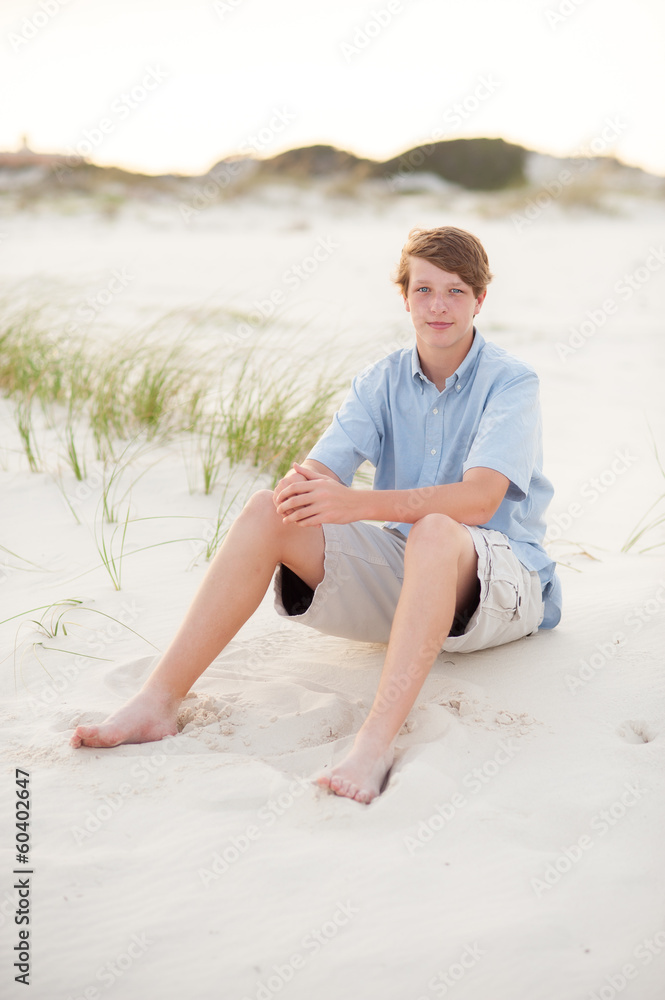 teen boy sitting in the sand on the beach