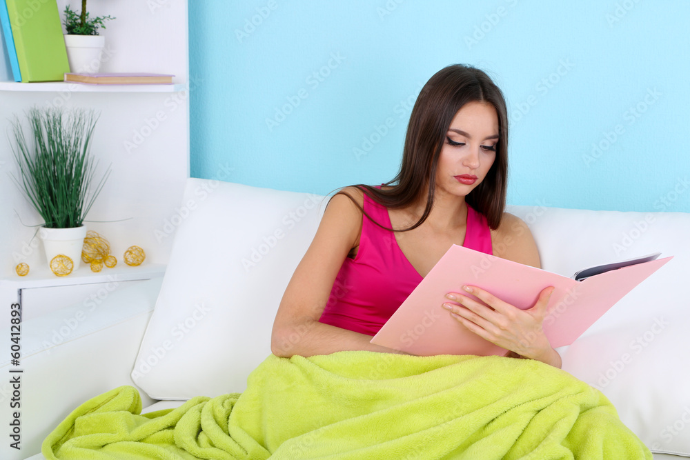 Beautiful young woman reading book on sofa on blue background Beautiful young woman reading book on sofa on blue background