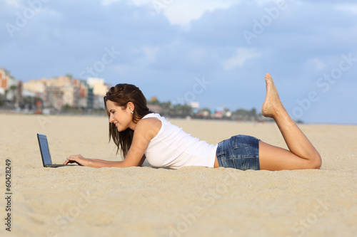 Teenager girl browsing her laptop lying on the sand of the beach