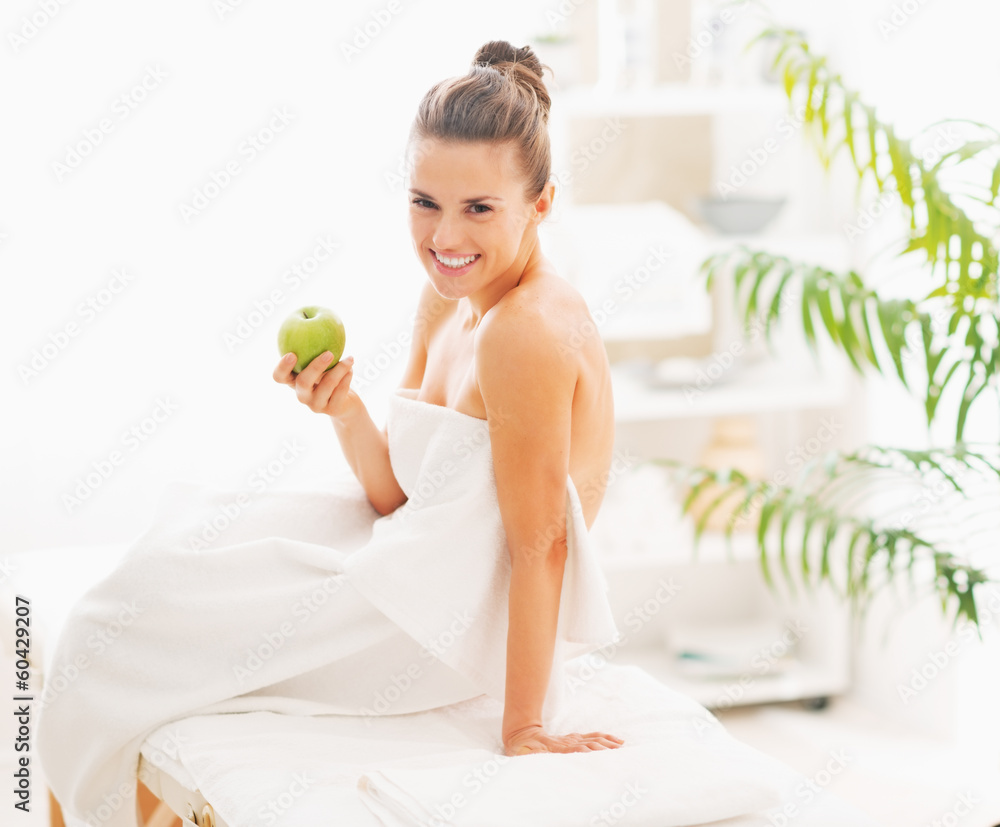 Smiling young woman with apple sitting on massage table Smiling young woman with apple sitting on massage table