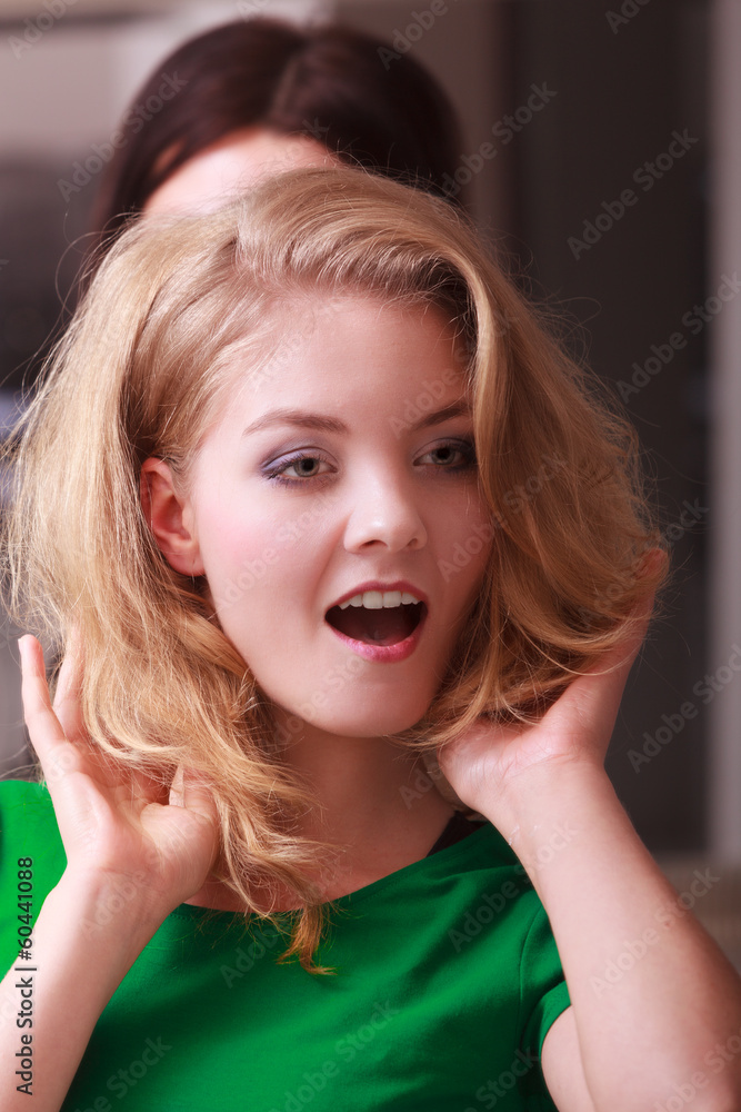 Fototapeta premium Smiling girl with blond wavy hair by hairdresser in beauty salon