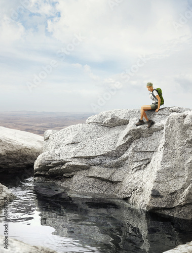 young traveler woman sitting on a rock near water