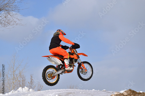 MX rider on the bike jumps from a hill on a snowy highway