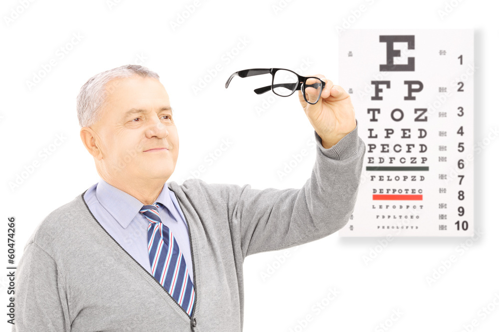 Senior gentleman standing in front of eyesight test holding a pa Senior gentleman standing in front of eyesight test holding a pa