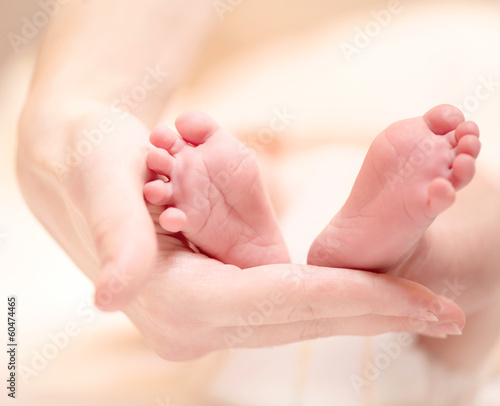 Tiny Newborn Baby's feet on female hands closeup.