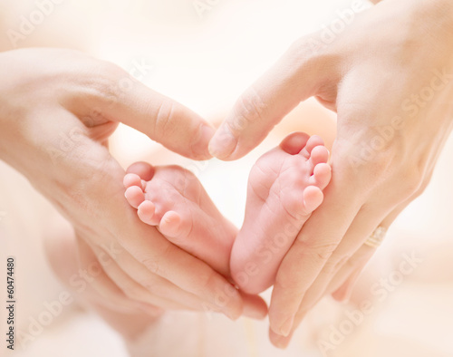 Tiny Newborn Baby s feet on female Heart Shaped hands closeup