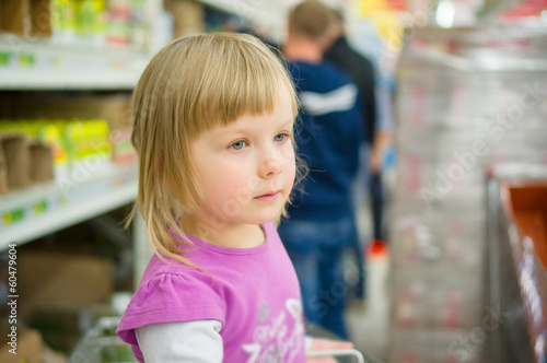 Adorable girl at shoppoing cart grimacing in supermarket