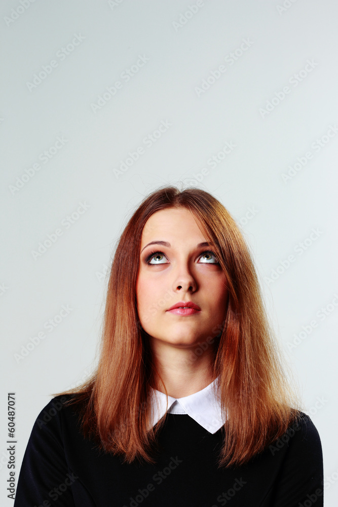 Young thoughtful woman looking up on gray background Young thoughtful woman looking up on gray background