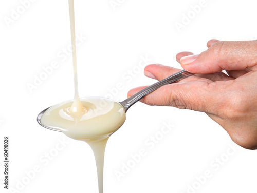 Female hand with a spoon pouring condensed milk