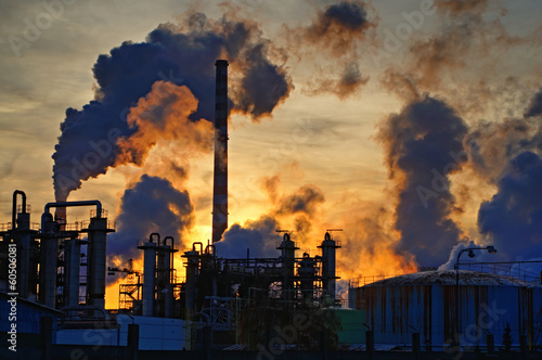Chimneys and dark smoke over chemical factory at sunset