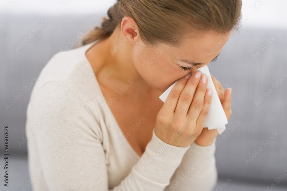 Young woman sitting on couch and blowing nose Young woman sitting on couch and blowing nose