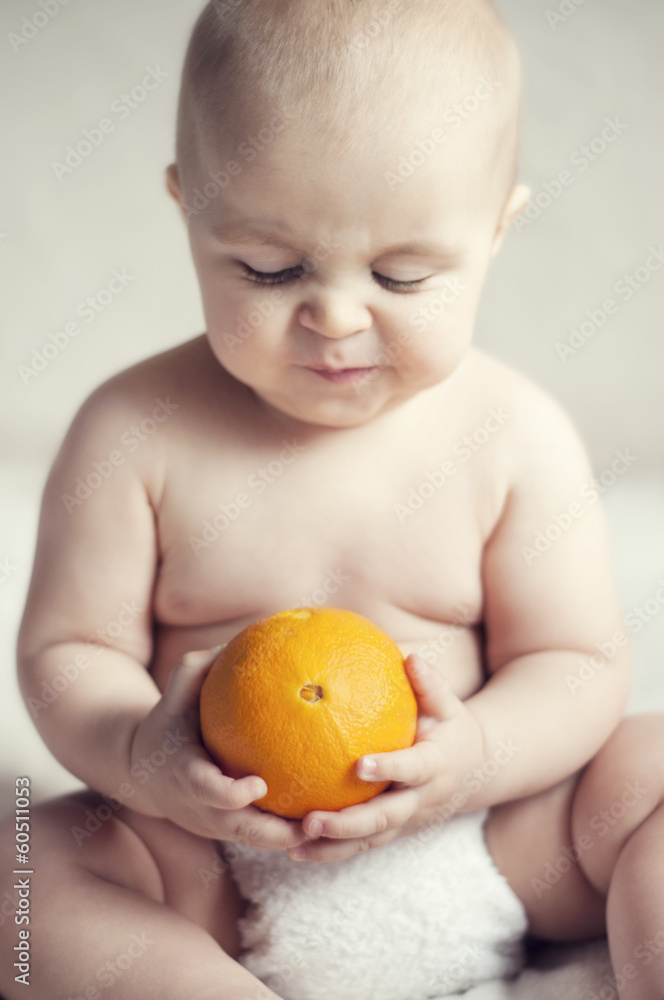 Cute baby sitting on the bed and watching an orange Cute baby sitting on the bed and watching an orange