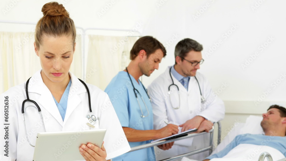 Doctors speaking with sick patient while one checks tablet Doctors speaking with sick patient while one checks tablet