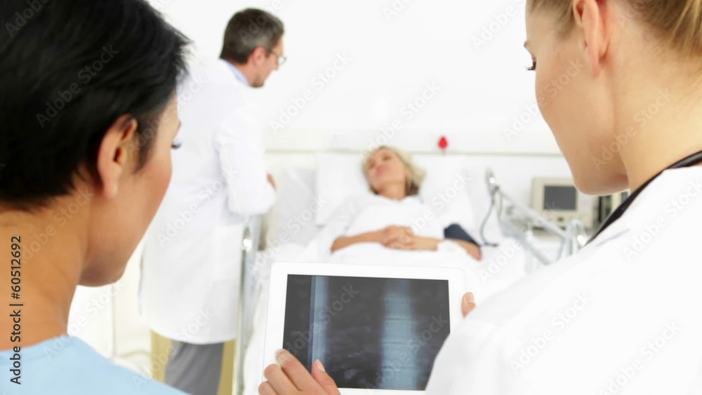 Doctors studying xrays on tablet in front of sick patient in bed Doctors studying xrays on tablet in front of sick patient in bed