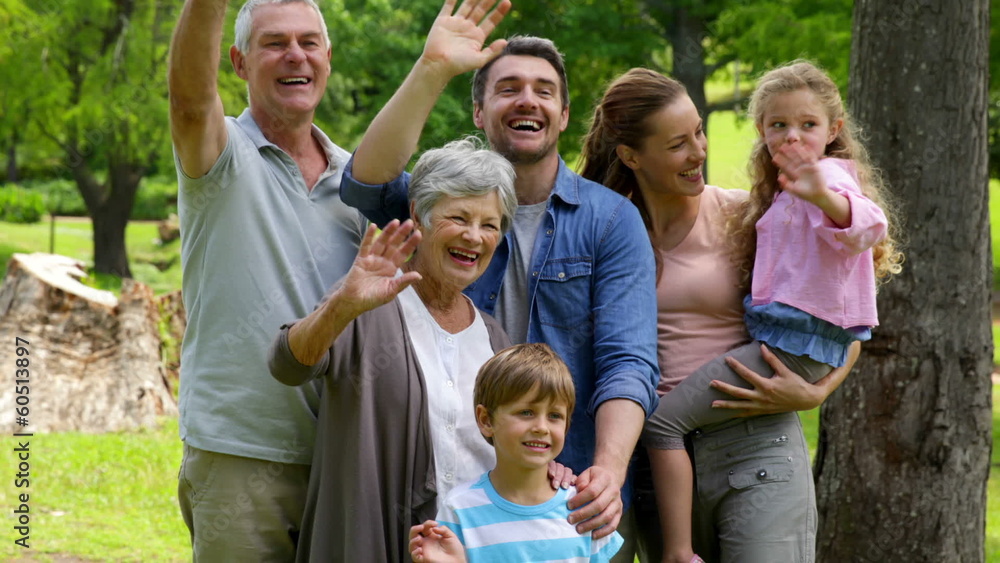 Multi generation family posing and waving at camera in a park Multi generation family posing and waving at camera in a park