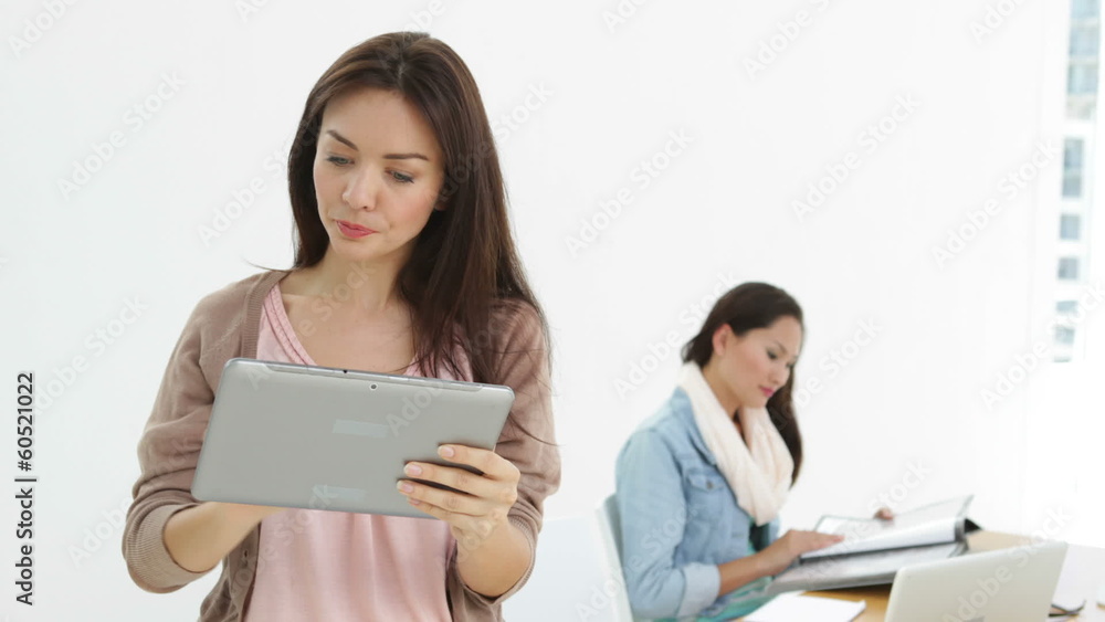 Creative businesswoman using tablet with colleague behind her Creative businesswoman using tablet with colleague behind her