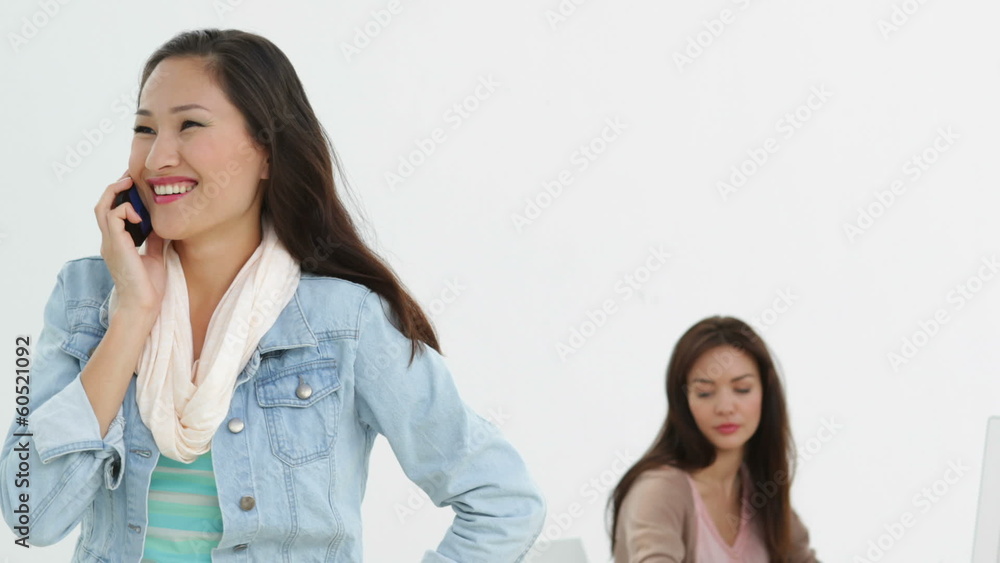 Creative businesswoman on the phone with coworker behind her Creative businesswoman on the phone with coworker behind her