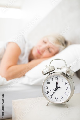 Woman sleeping in bed with alarm clock in foreground at bedroom