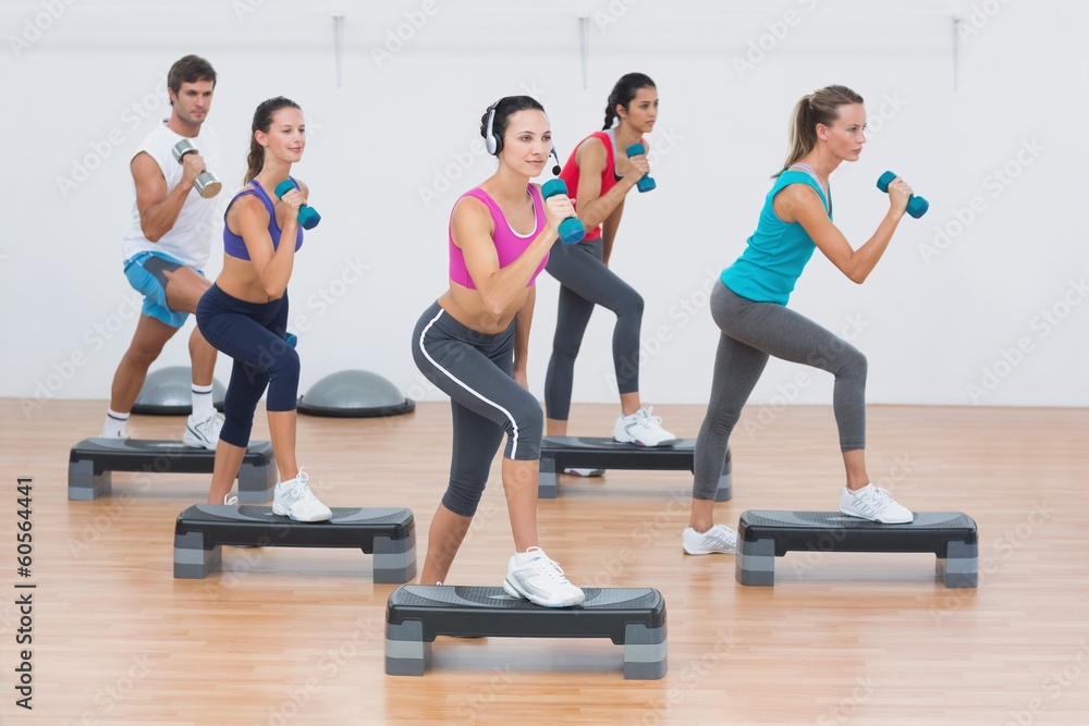 Fototapeta premium Fitness class performing step aerobics exercise with dumbbells